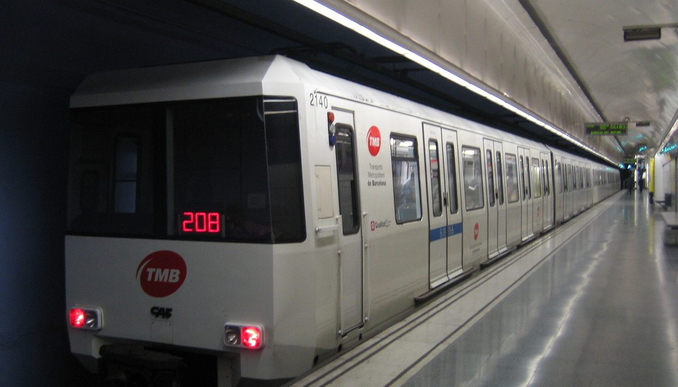White TMB series 2000 metro train with red logo stopped at a bright underground Barcelona station platform