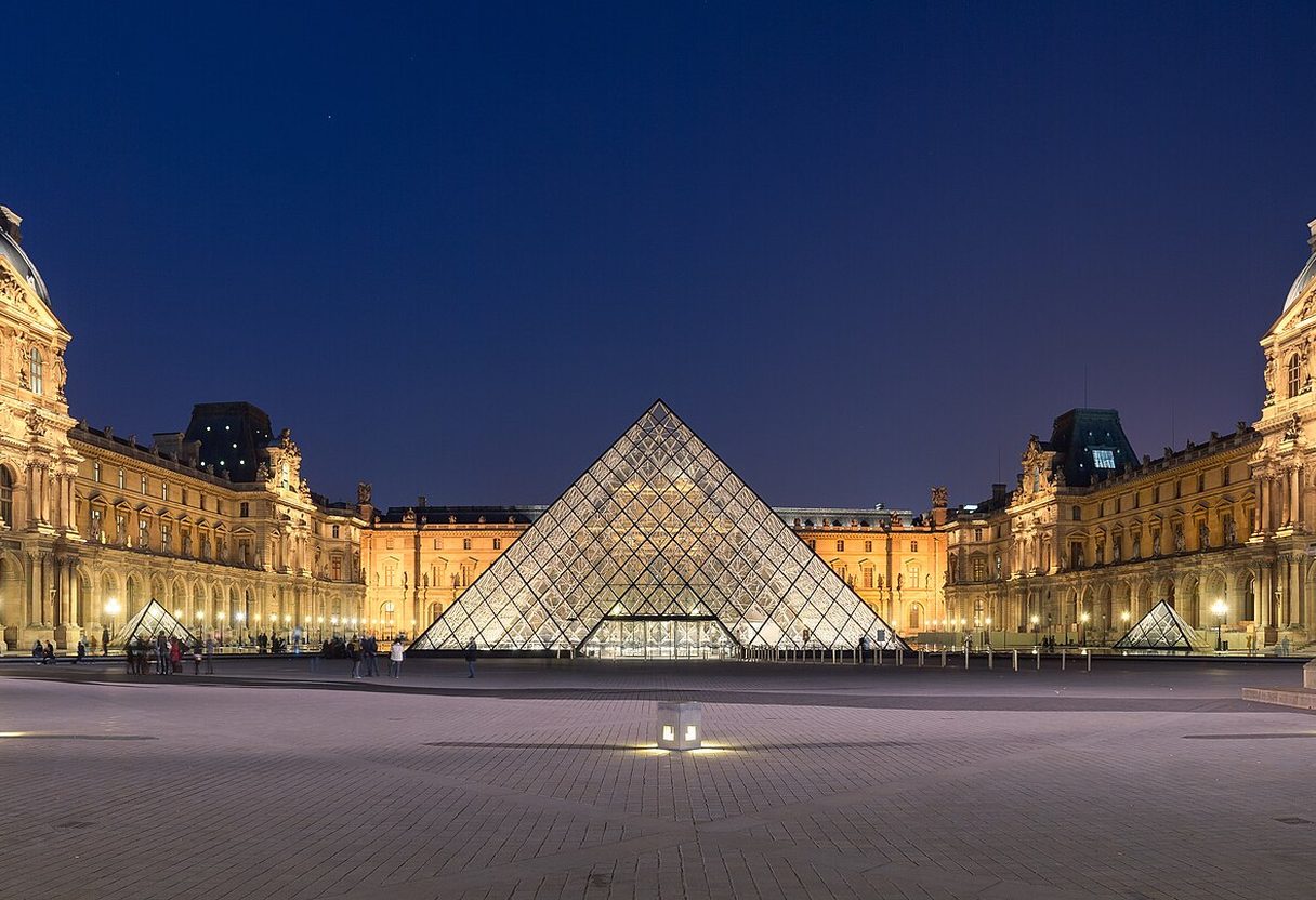 Illuminated Louvre glass pyramid at dusk, framed by the palace wings and an equestrian statue in Cour Napoléon