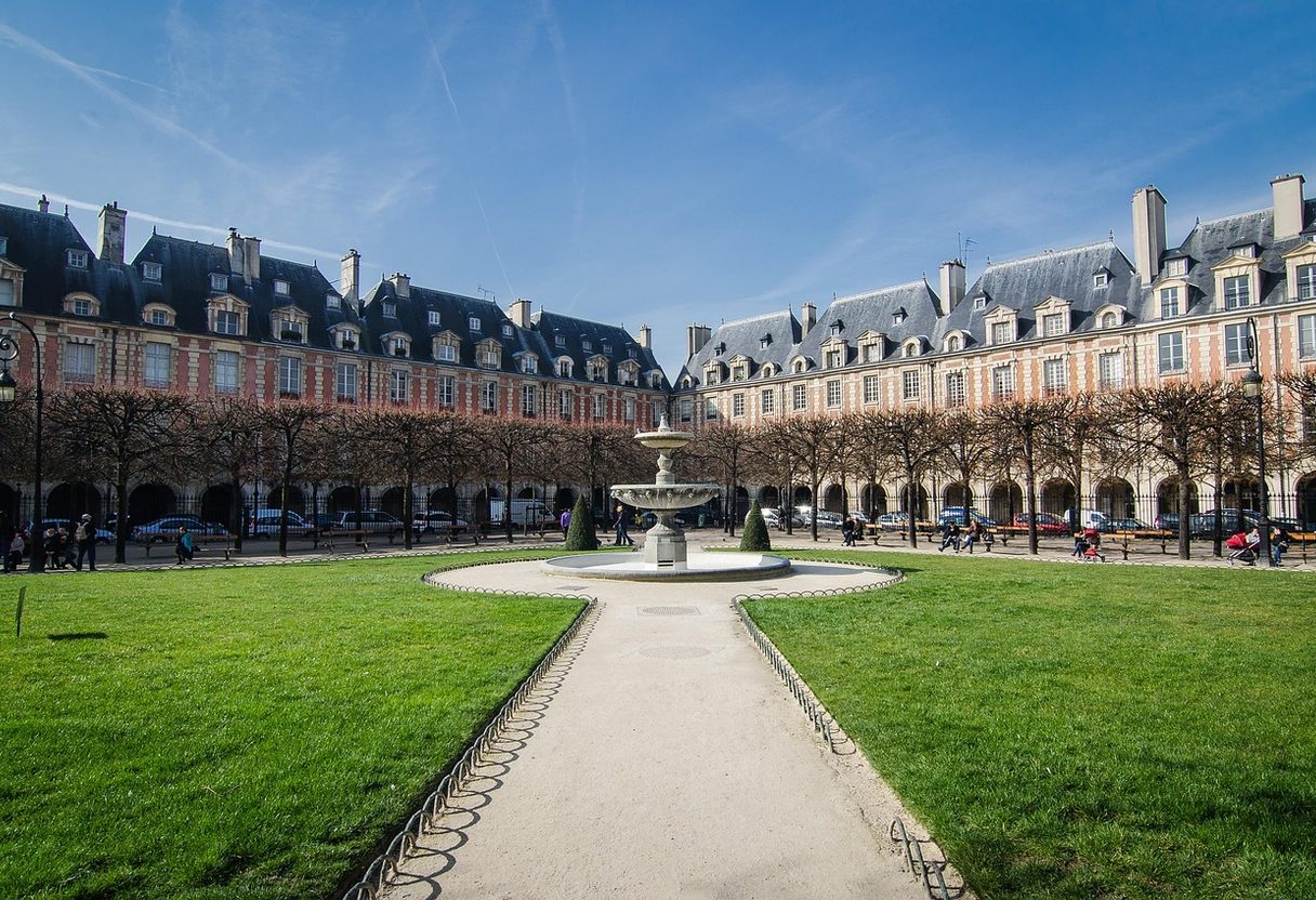 Place des Vosges with central fountain, green lawns and red-brick arcaded townhouses under a blue sky