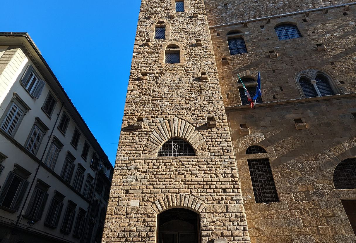 Stone tower and crenellated facade of the Bargello palace in Florence under a clear blue sky