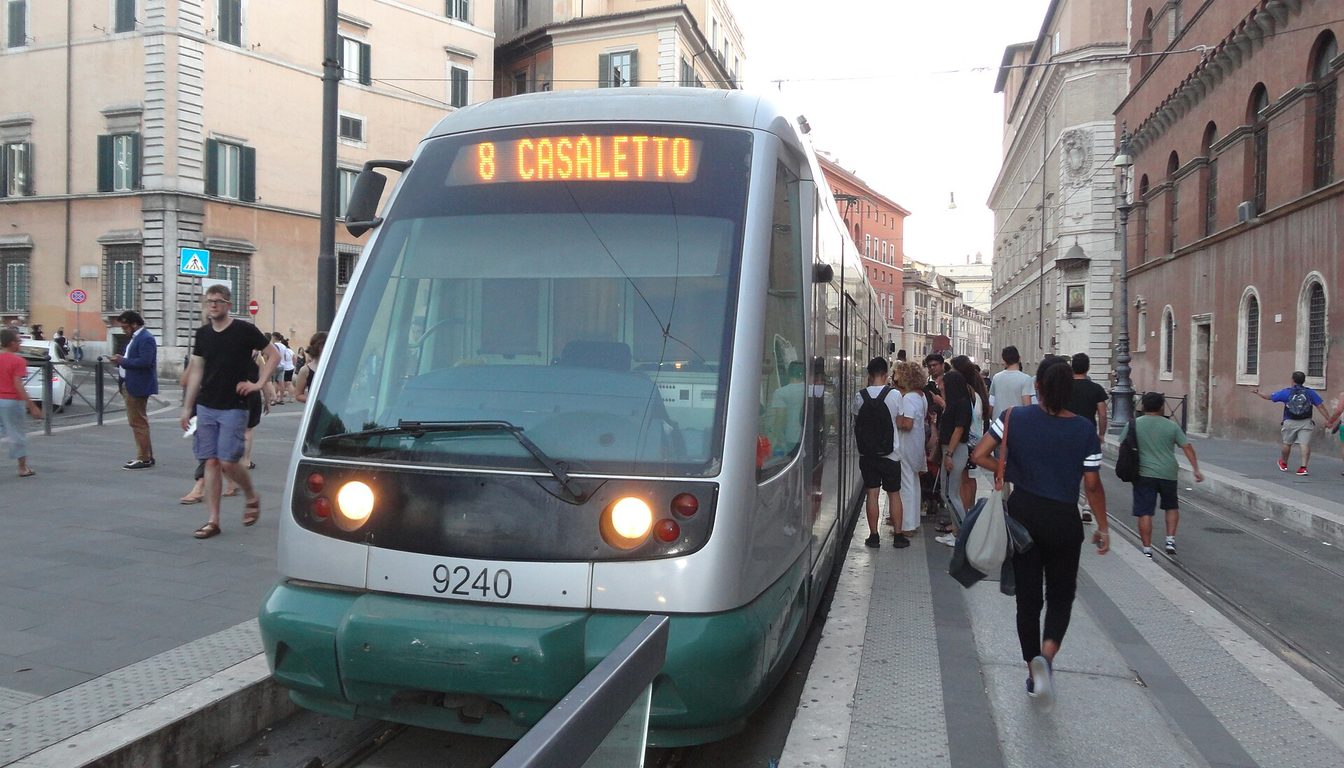 Line 8 tram to Casaletto at a busy stop in central Rome, framed by historic ochre buildings