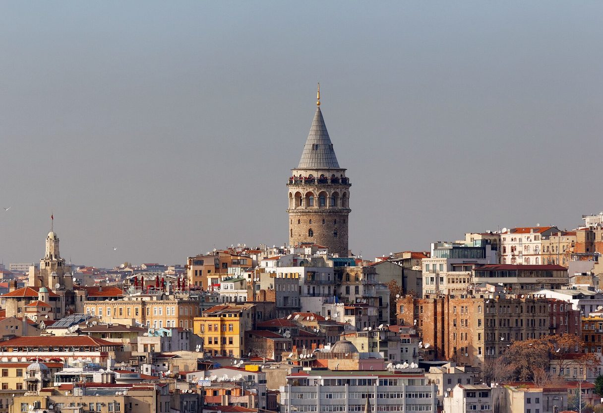 Galata Tower's stone cylinder and conical roof rising above the dense rooftops of Beyoğlu in soft daylight