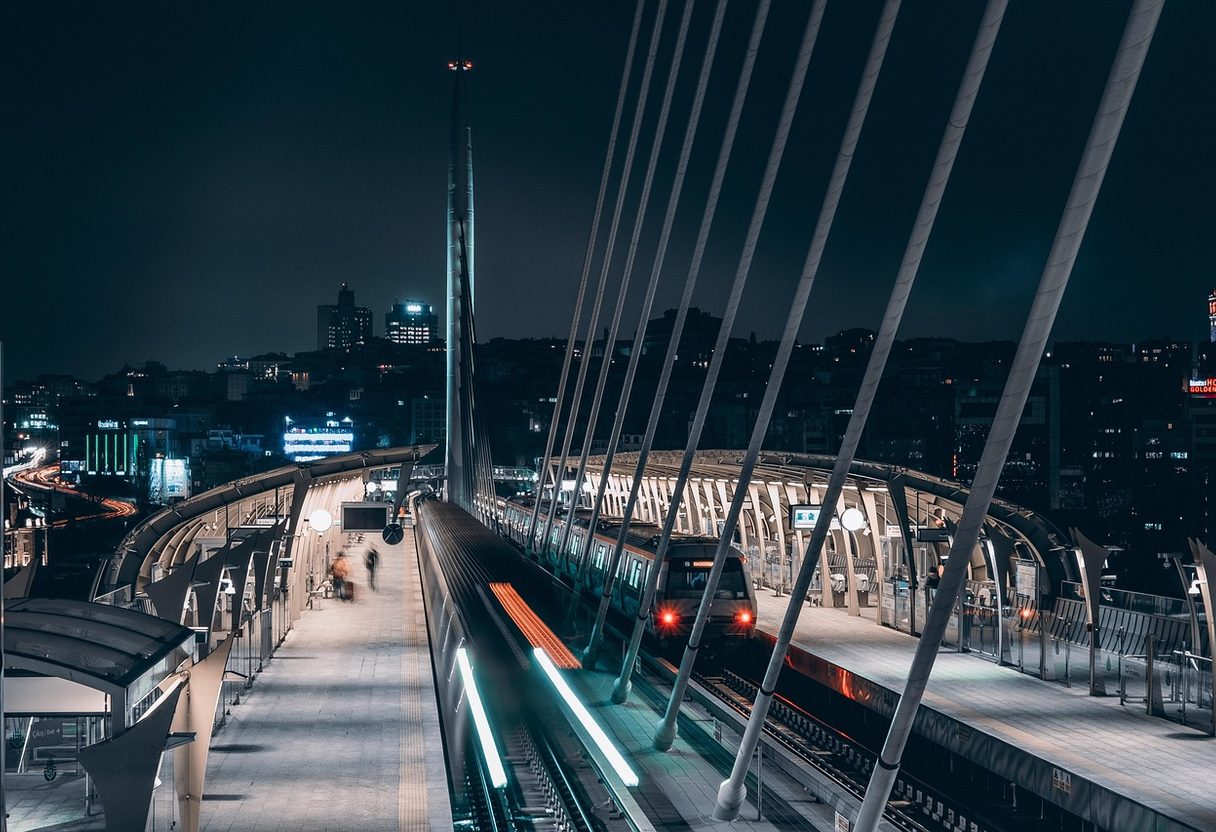 Metro train arriving at the Golden Horn Bridge station at night with Istanbul city lights behind