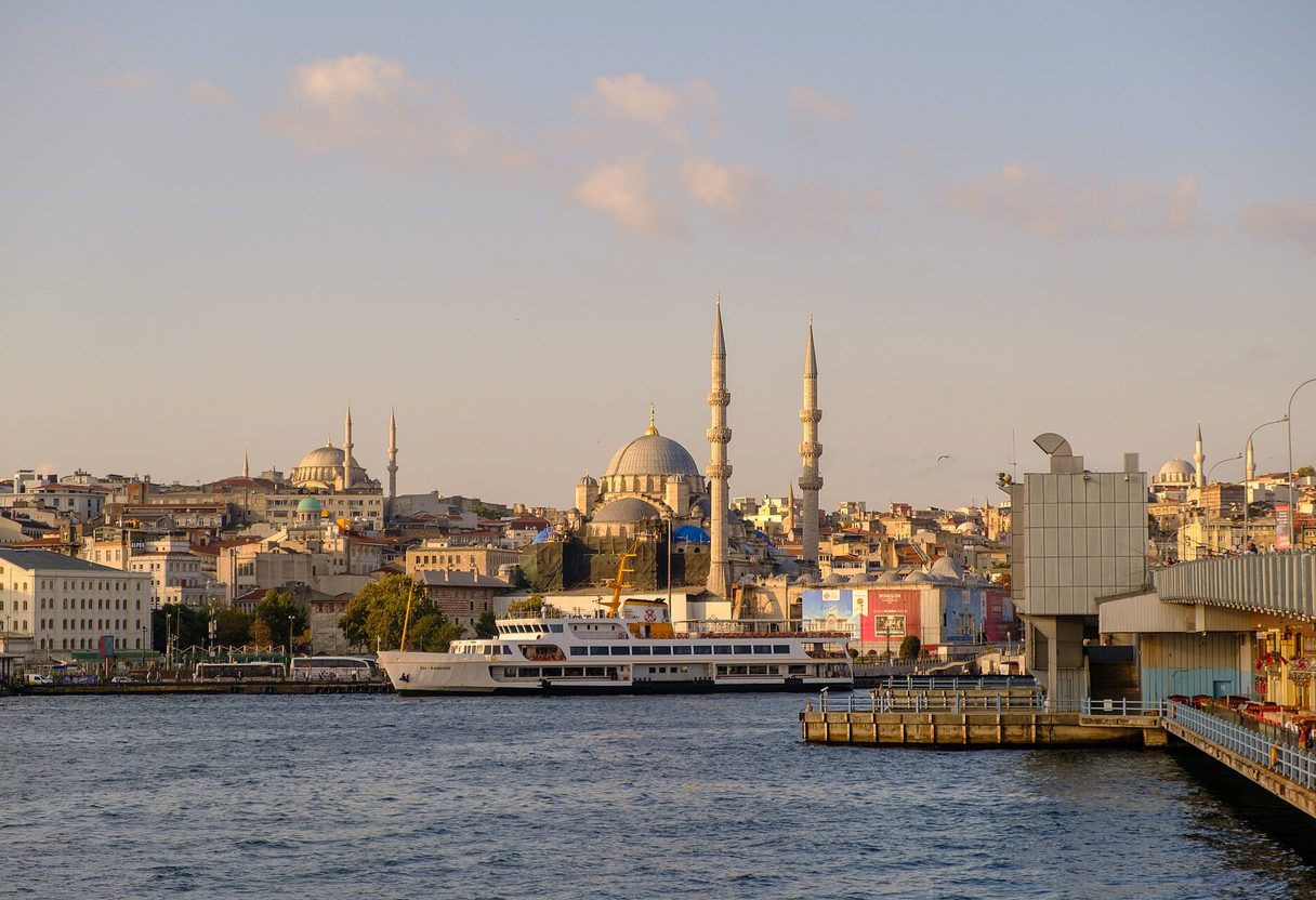 White ferry docked on the Eminönü waterfront below the Yeni Cami and Süleymaniye Mosque at golden hour