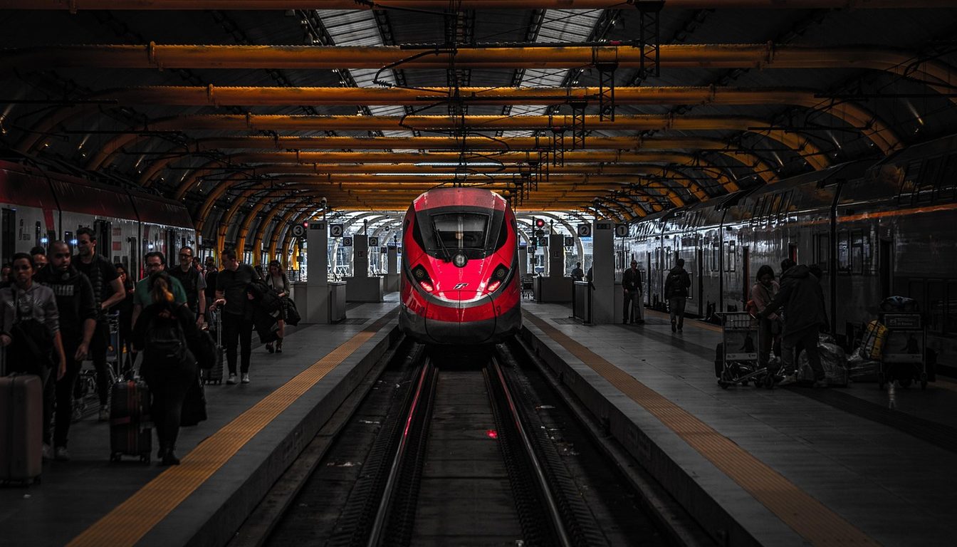 Red Frecciarossa high-speed train arriving under a station canopy with passengers on both platforms