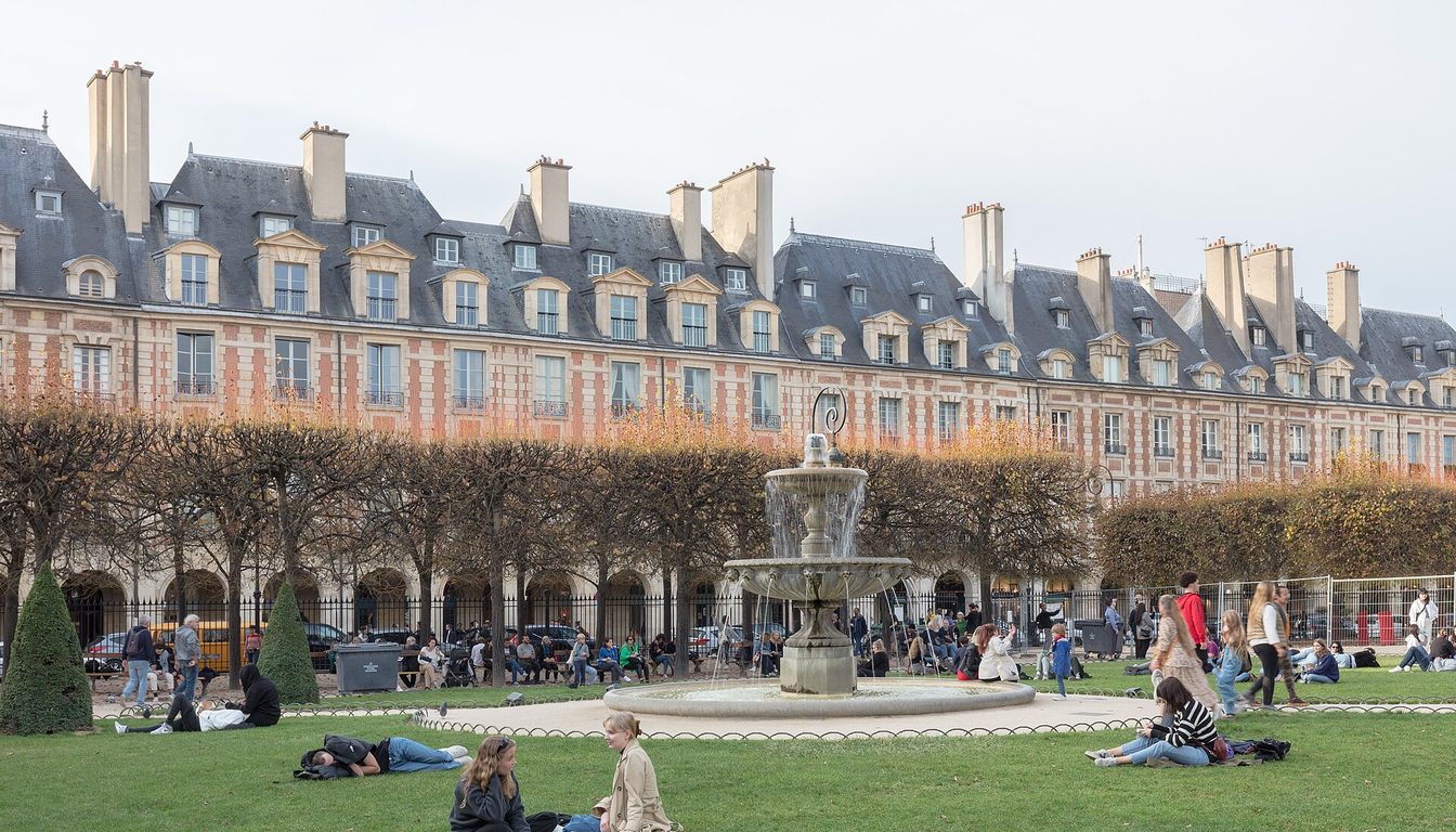 Red-brick arcaded pavilions around Place des Vosges with fountain, trimmed trees and people on the lawn
