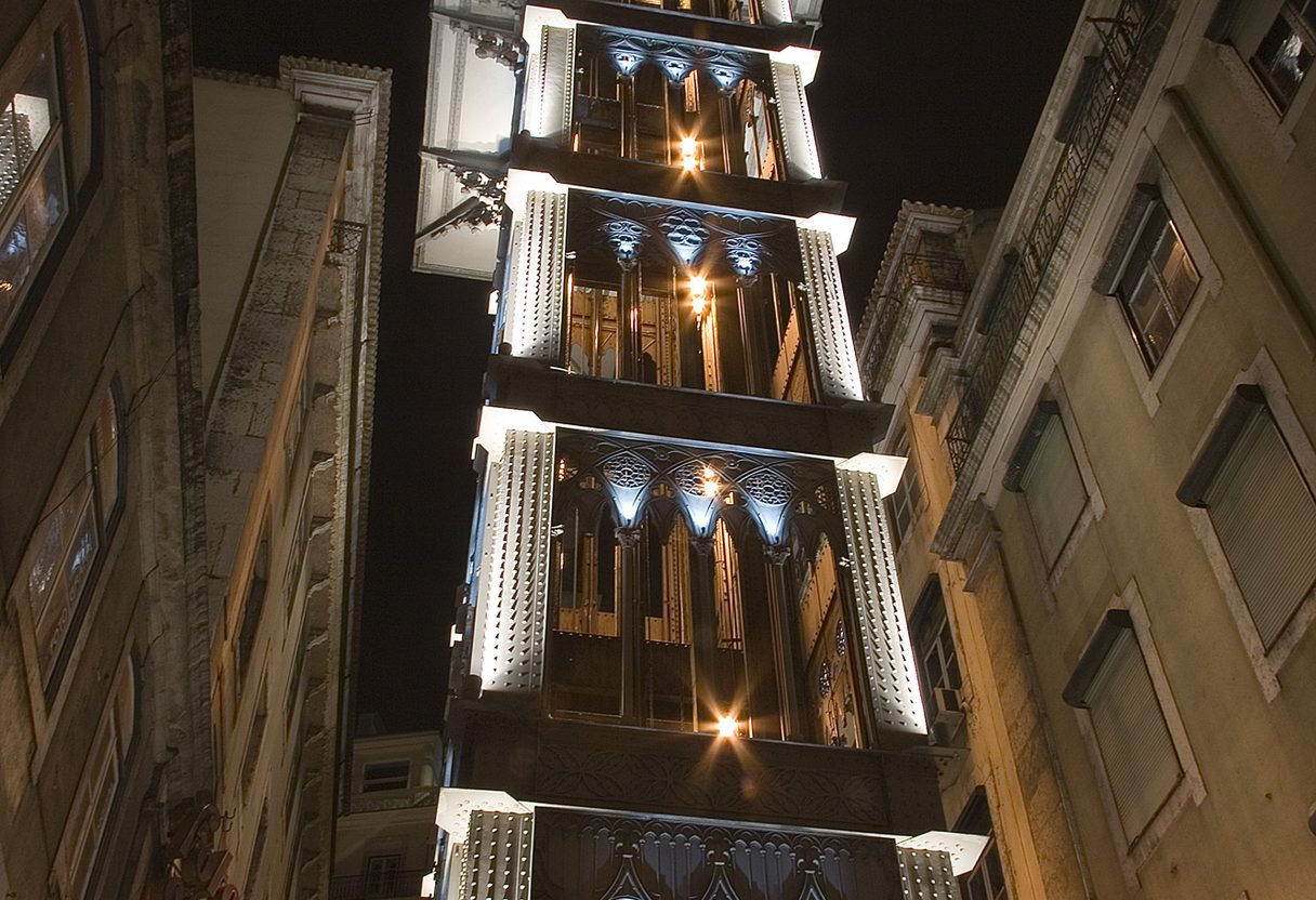 Elevador de Santa Justa lit up at night, seen from below between dark building facades in Baixa, Lisbon