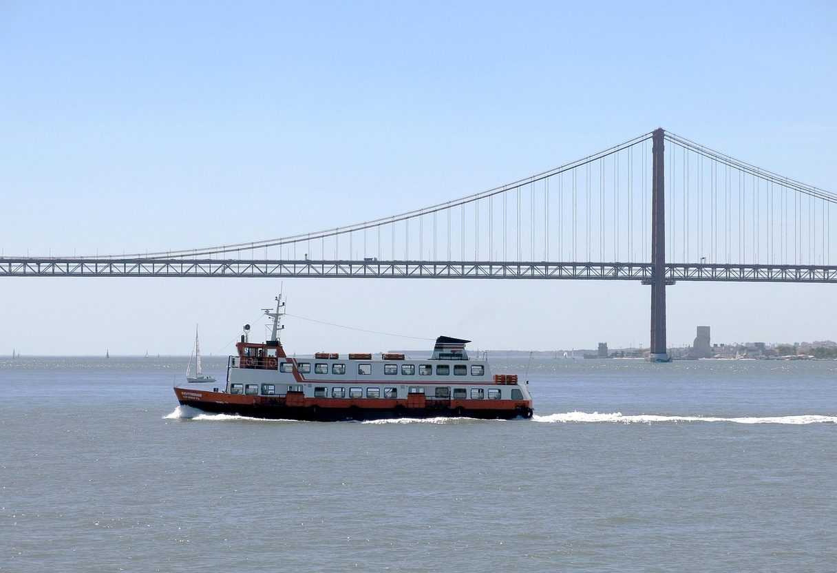 Orange and white commuter ferry crossing the Tagus with the 25 de Abril suspension bridge behind