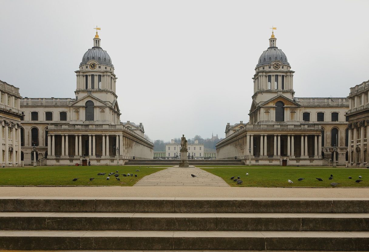 Twin domed baroque buildings of the Old Royal Naval College in Greenwich framing a lawn, statue and the Queen's House beyond