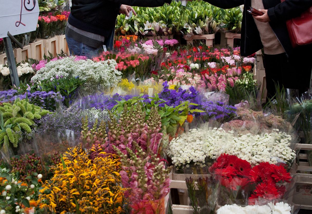 Vendor handing a wrapped bouquet to a customer over buckets of colourful cut flowers at Columbia Road market