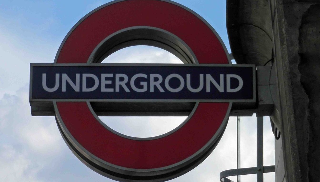 Classic red-and-blue London Underground roundel sign mounted on a stone building against a blue sky