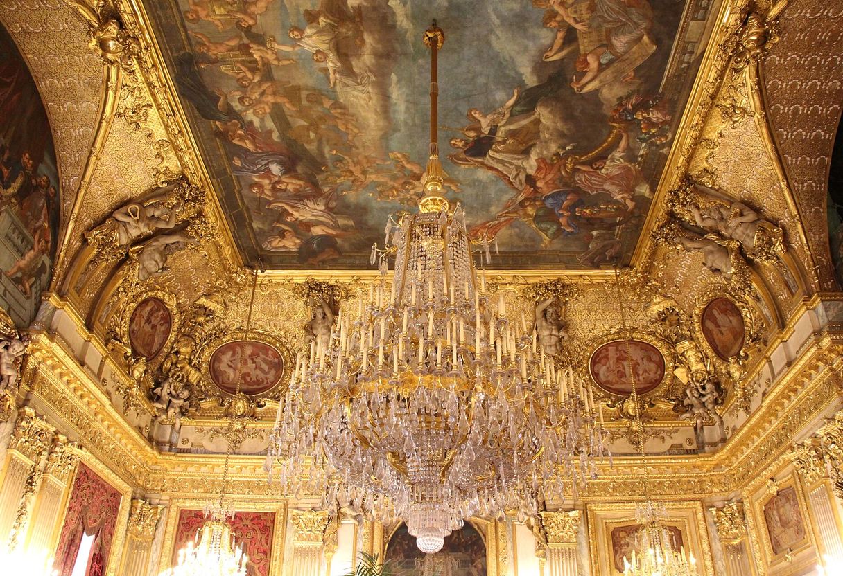Massive crystal chandelier beneath a painted ceiling framed by lavish gilded mouldings and medallions