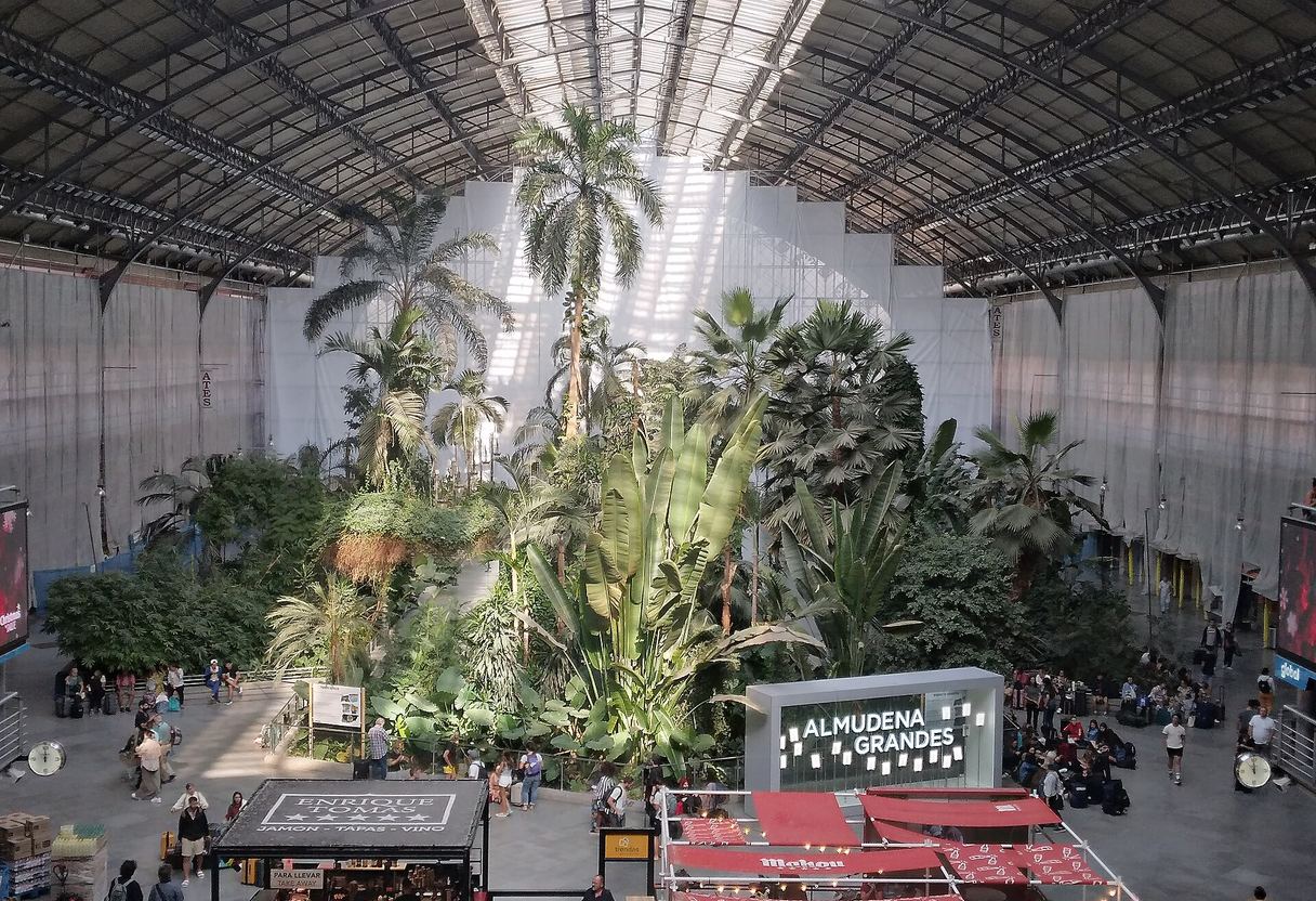 Tropical palms and plants filling the iron-and-glass hall of Madrid Atocha station, with travellers and cafés around