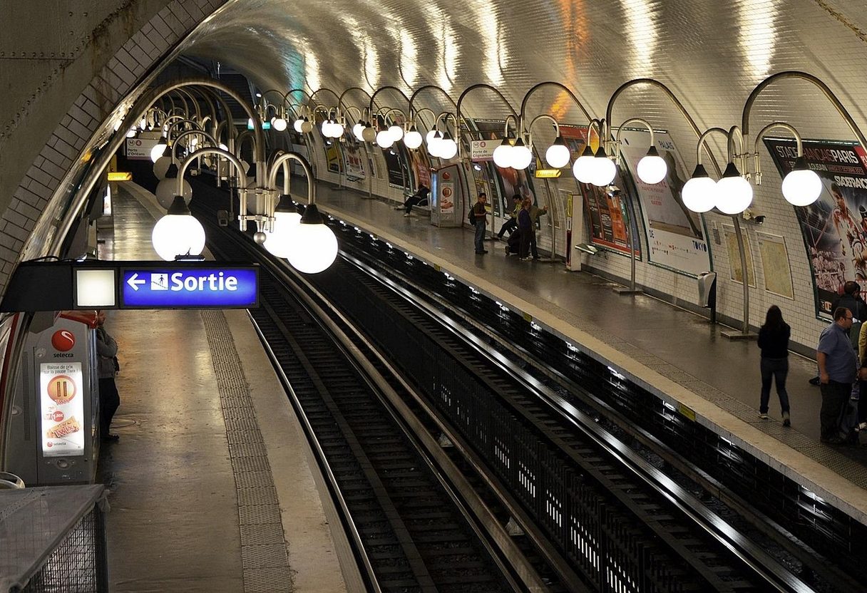 Paris Métro Cité station with globe lamps over the tracks and a blue Sortie sign with arrow on the platform