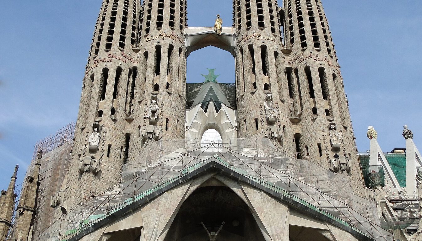 Sagrada Família Passion facade with four tall spires and angular stone columns under a blue sky
