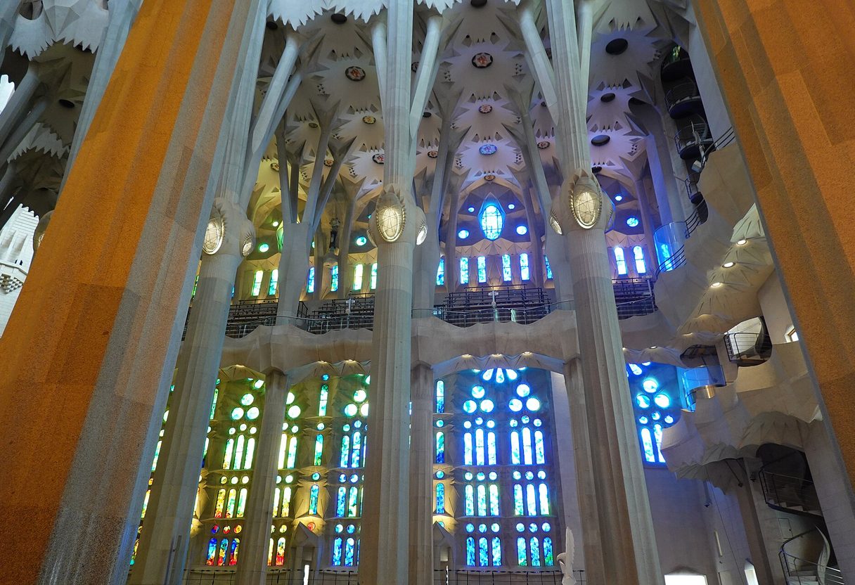 Sagrada Família nave with tree-like columns and green and blue stained glass windows filling the interior with coloured light