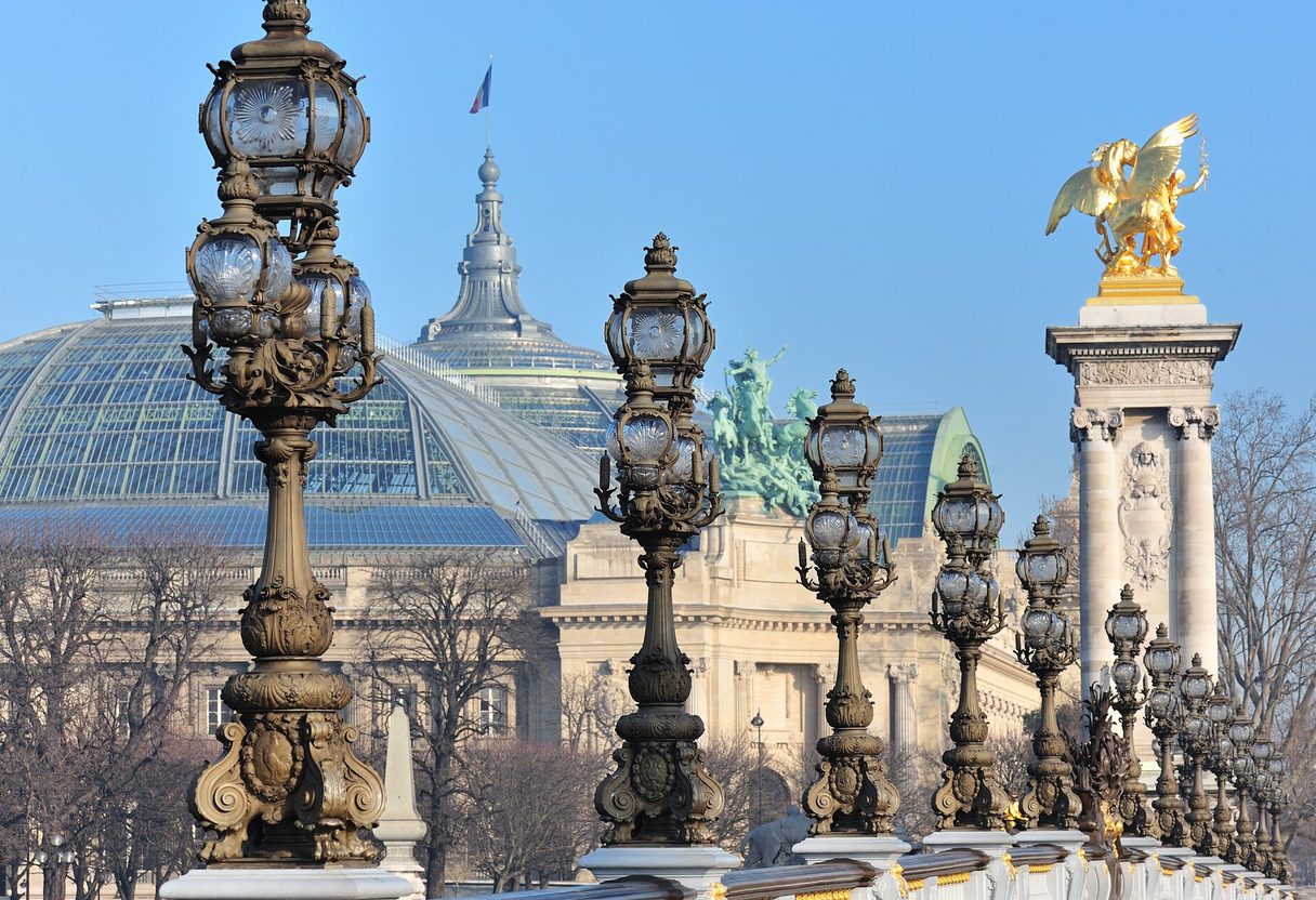 Ornate bronze lampposts and a gilded Pegasus column on Pont Alexandre III, with the Grand Palais glass roof behind