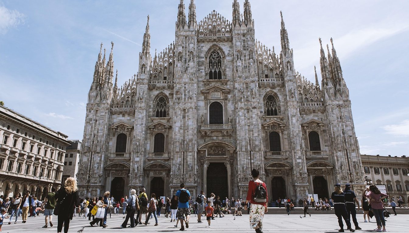 Tourists walking across Piazza del Duomo in front of the Gothic facade of Milan Cathedral on a sunny day