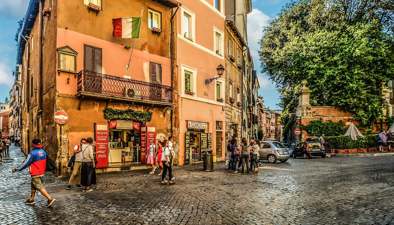 Cobbled Trastevere square with an Italian flag on a pink building, cafés and people strolling in warm light